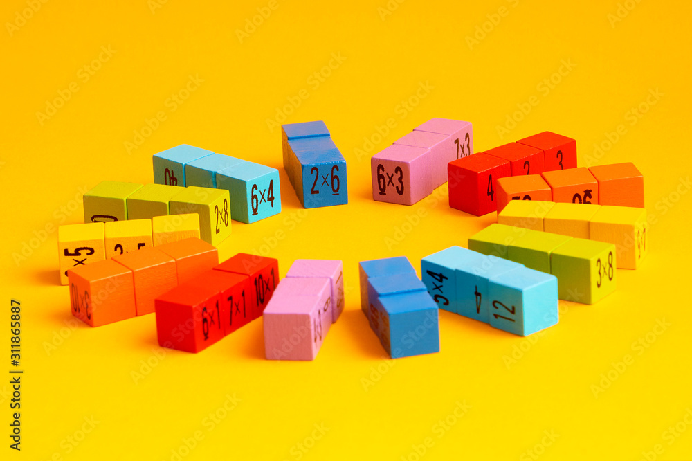 Multicolored wooden cubes with a multiplication table on the sides. Laid out in the shape of the sun, on a yellow monochrome isolated background. Copy space. School education. Selective focus.
