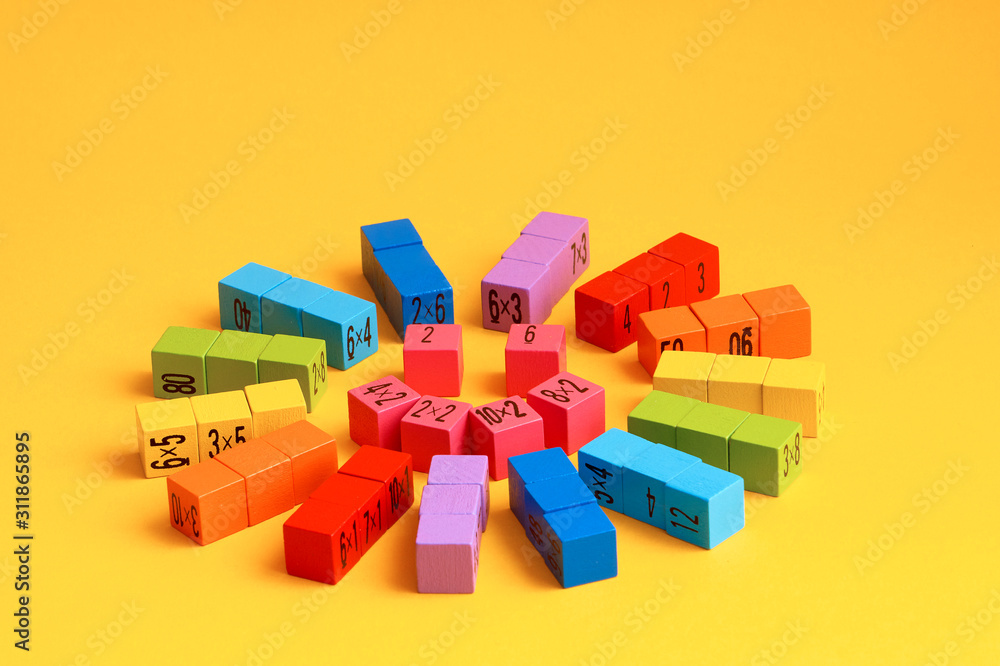 Naklejka premium Multicolored wooden cubes with a multiplication table on the sides. Laid out in the shape of a smiling sun, on a yellow monochrome isolated background. Copy space. School education. Selective focus.