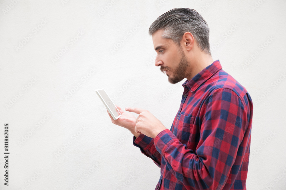 Side view of serious bearded man using tablet pc. Concentrated bearded man in checkered shirt design digital tablet on grey background. Wireless technology concept Side view of serious bearded man using tablet pc. Concentrated bearded man in checkered shirt design digital tablet on grey background. Wireless technology concept