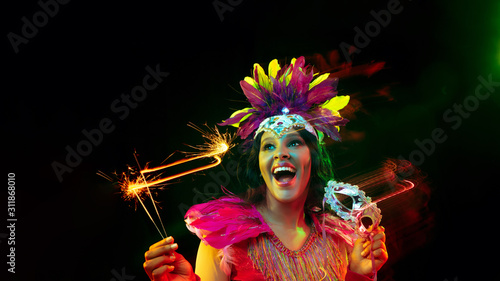 Fotografia Beautiful young woman in carnival mask, stylish masquerade costume with feathers and sparklers inviting