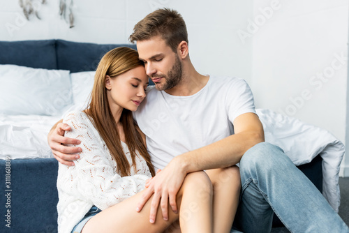 handsome man hugging attractive woman with closed eyes in apartment