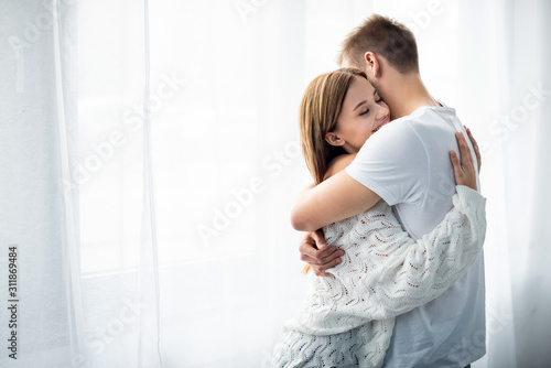 man hugging attractive and smiling woman in apartment