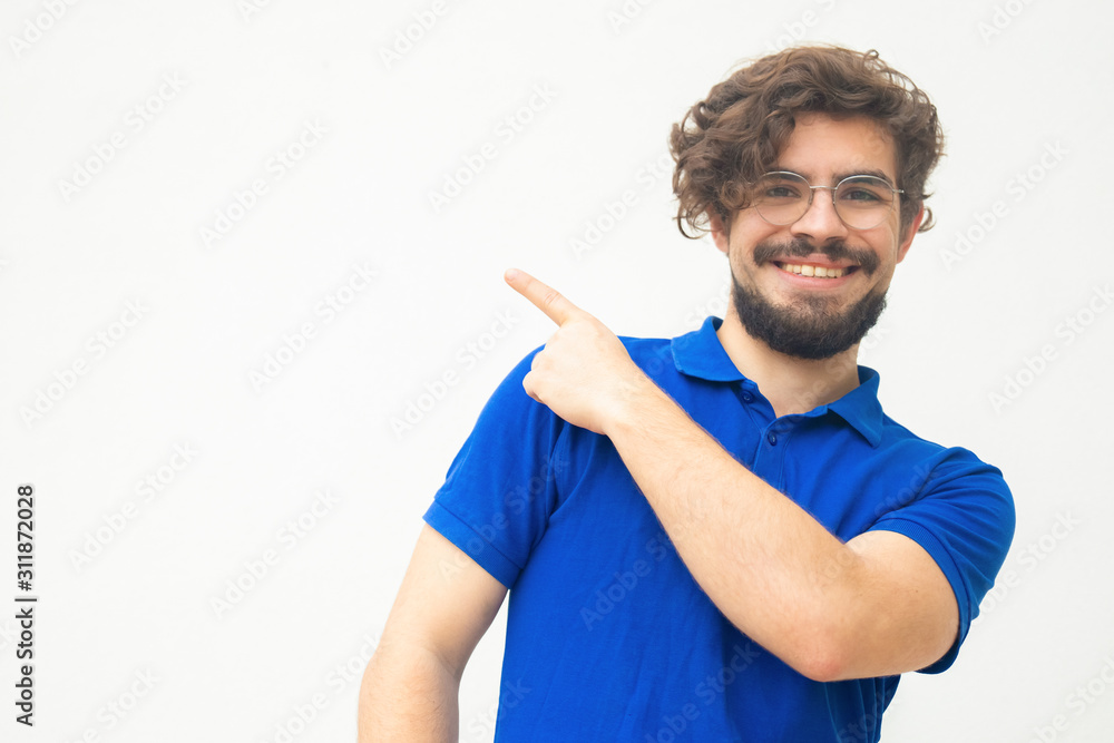 Happy cheerful guy pointing finger away at copy space. Handsome bearded young man in blue casual t-shirt posing isolated over white background. Advertising concept Happy cheerful guy pointing finger away at copy space. Handsome bearded young man in blue casual t-shirt posing isolated over white background. Advertising concept