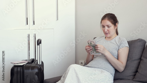 Young woman is planning vacation budget distributing money for necessary purches. She lays out the cash bills sitting on the couch. photo