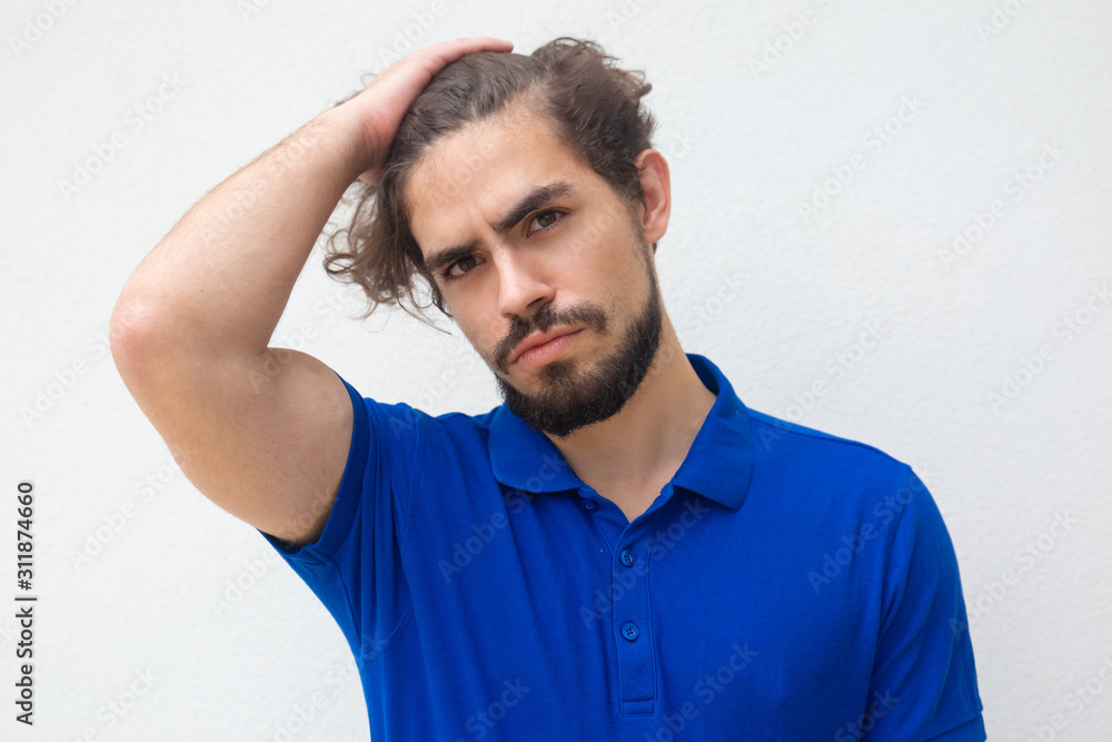 Pensive attractive guy touching head, doing up hair, looking at camera. Handsome bearded young man in blue casual t-shirt posing isolated over white background. Closeup male portrait concept Pensive attractive guy touching head, doing up hair, looking at camera. Handsome bearded young man in blue casual t-shirt posing isolated over white background. Closeup male portrait concept