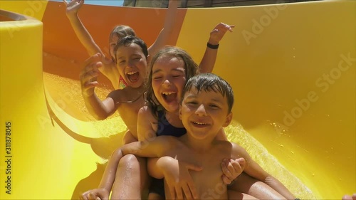 Happy children are riding down a slide in an aquapark. Children laugh merrily and wave their hands