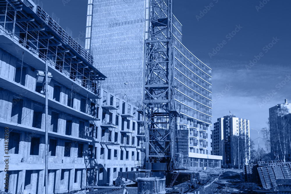 Crane and building construction site against blue sky, toned trendy classic blue color of year 2020