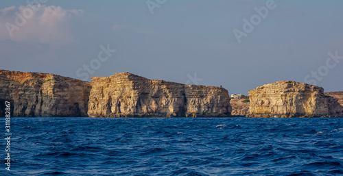 Rocky edges of the Comino island sticking out from Mediterranean Sea and lit by the orange evening sun. Rock formations with caves.