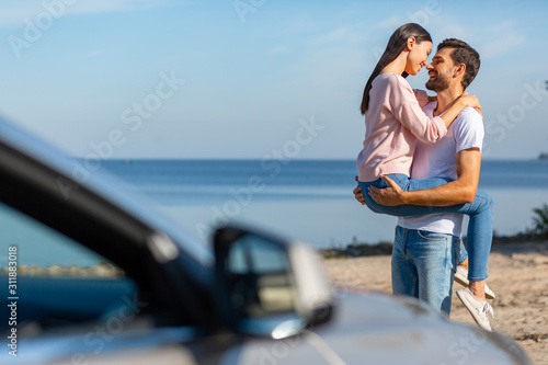 asian woman in love looking at her boyfriend holding her on the hands with car in foreground © Afshar Tetyana