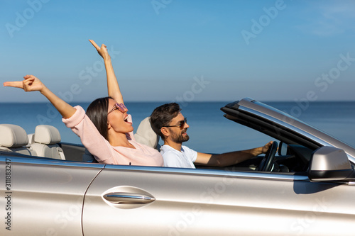 Foto side view of happy woman holding hands up sitting in cabriolet with boyfriend