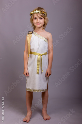 Cute child dressed like ancient roman god. Mascarade costume for holidays. Studio shot gray background