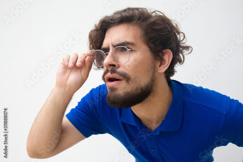 Closeup of focused attentive guy in glasses staring away with open mouth. Handsome bearded young man in blue casual t-shirt posing isolated over white background. Unbelievable news concept
