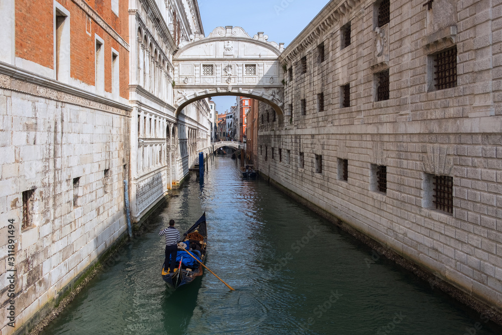Narrow canal between buildings, arched bridge, gondola on the water. Venice, Italy.