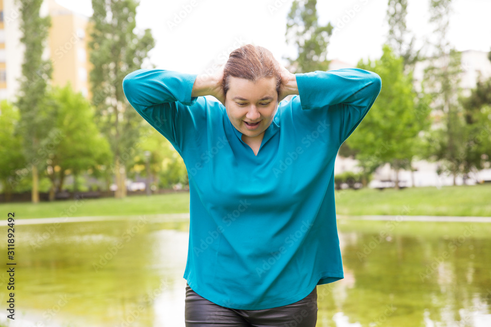 Focused cheerful woman walking in park, doing light exercises, stretching neck. Middle aged woman in casual posing outdoors. Active walk concept Focused cheerful woman walking in park, doing light exercises, stretching neck. Middle aged woman in casual posing outdoors. Active walk concept