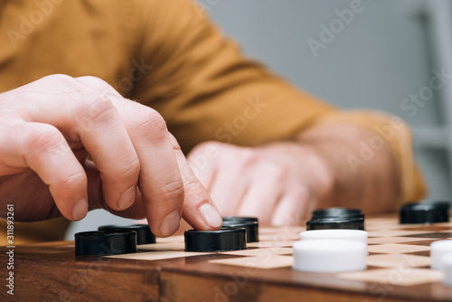 Cropped view of man playing checkers on wooden checkerboard