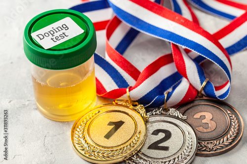 Doping test. Gold, silver and bronze medal and a jar for urine analysis on a gray background