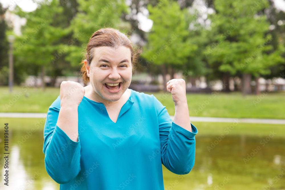 Joyful excited woman celebrating triumph, making winner gesture. Middle aged woman in casual posing outdoors. Winning prize concept Joyful excited woman celebrating triumph, making winner gesture. Middle aged woman in casual posing outdoors. Winning prize concept