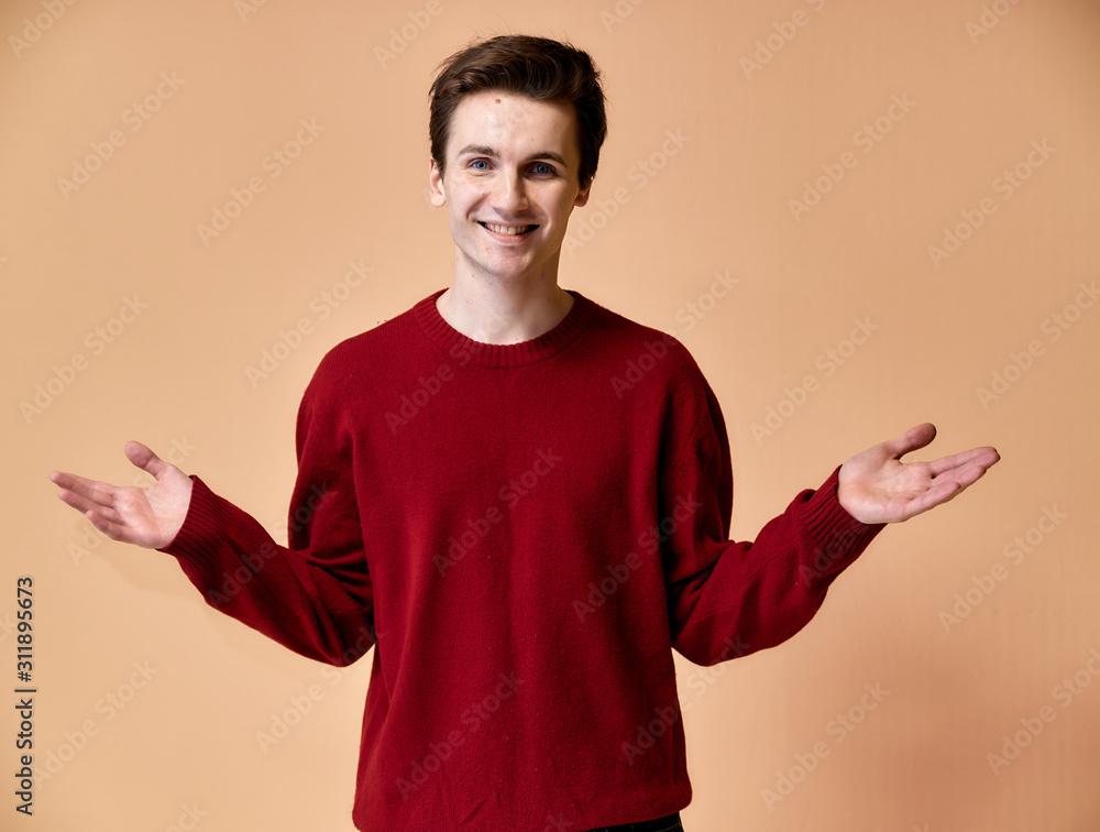 Portrait of a young Caucasian man with short hair and a white-toothed smile in a burgundy sweater on a pink background. Standing and talking right in front of the camera showing hands. Portrait of a young Caucasian man with short hair and a white-toothed smile in a burgundy sweater on a pink background. Standing and talking right in front of the camera showing hands.