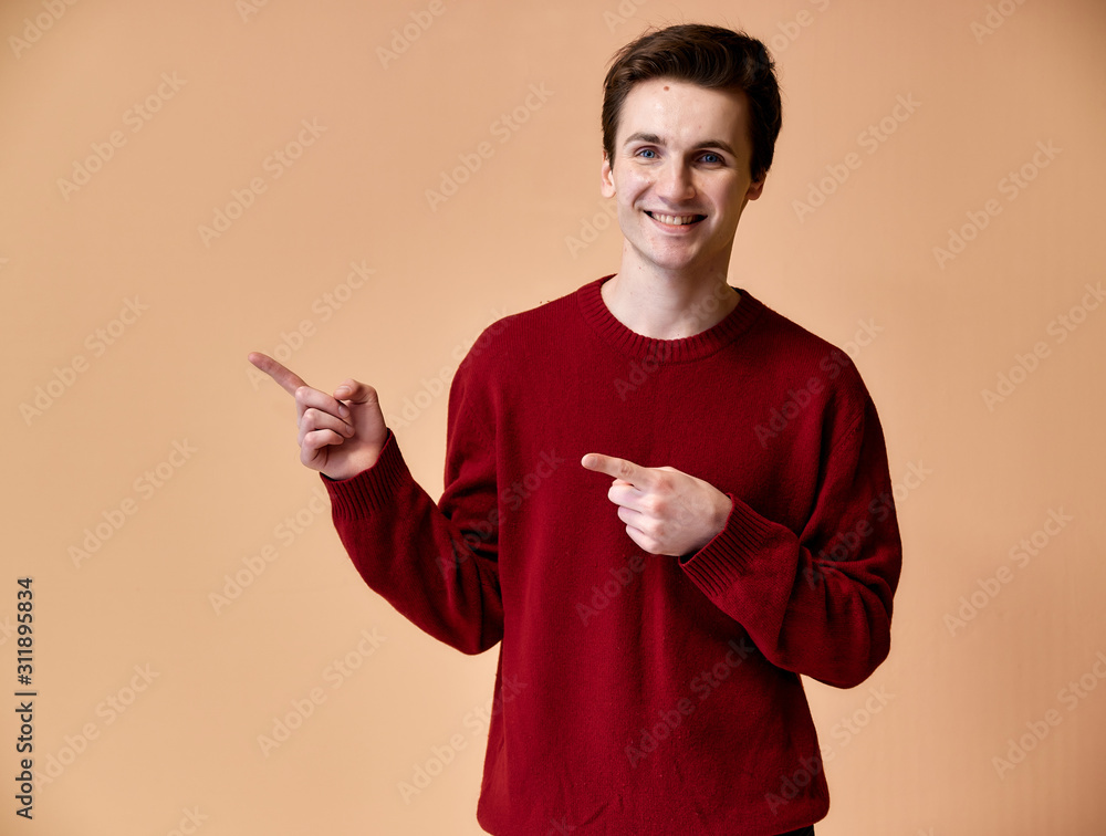 Portrait of a young Caucasian man with short hair and a white-toothed smile in a burgundy sweater on a pink background. Standing and talking right in front of the camera showing hands.