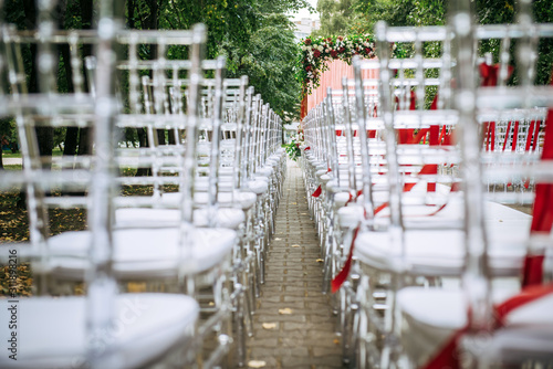 White plastic chairs decorated with red ribbons before the wedding ceremony outdoor. Rows of chairs, close-up selective focus. Abstract image.