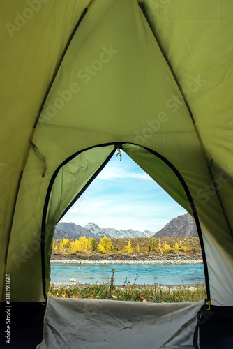 View from the tourist tent on beautiful landscape with turquoise river and high mountains under blue sky. Camping at mountain. Inside the green tent, vertical image with copy space.