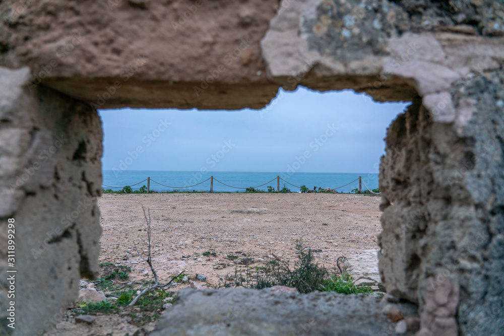 Coast seascape with the horizon skyline, through a window of an old ruined wall built in stone. Location: Sa Rapita, Campos, Balearic Islands, Spain.