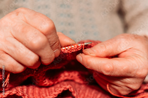 Older woman hands, knitting red sweater. Hobby and leisure