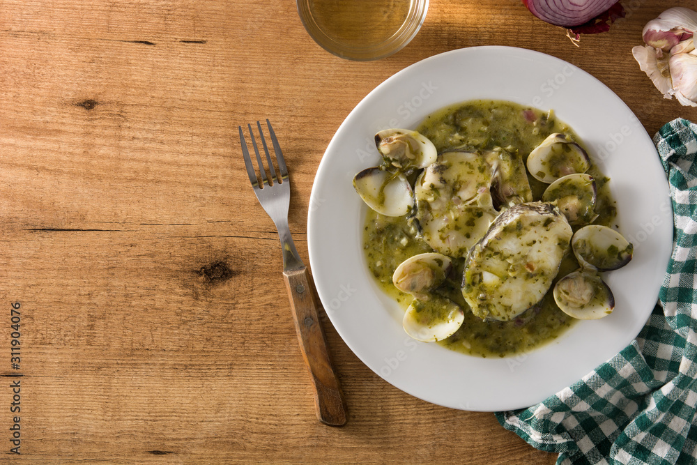 Hake fish and clams with green sauce on wooden table. Typical spanish recipe. Hake fish and clams with green sauce on wooden table. Typical spanish recipe.