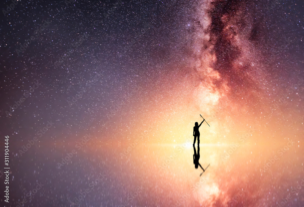 Fototapeta premium Beautiful starry night, hikers silhouette stands on and looks at the reflected Milky Way galaxy.