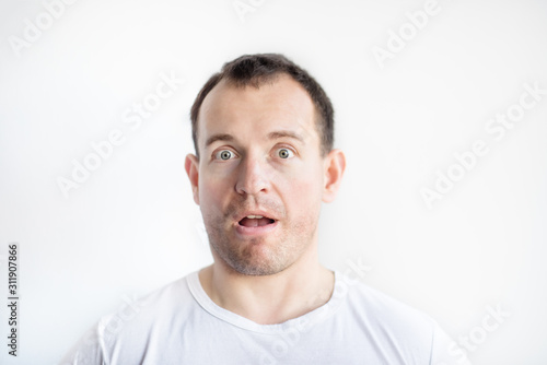 Closeup portrait of astonished surprised 30 years old caucasian white man on white background in white t-shirt with stubble on face. Lifestyle. Expressions on man face.