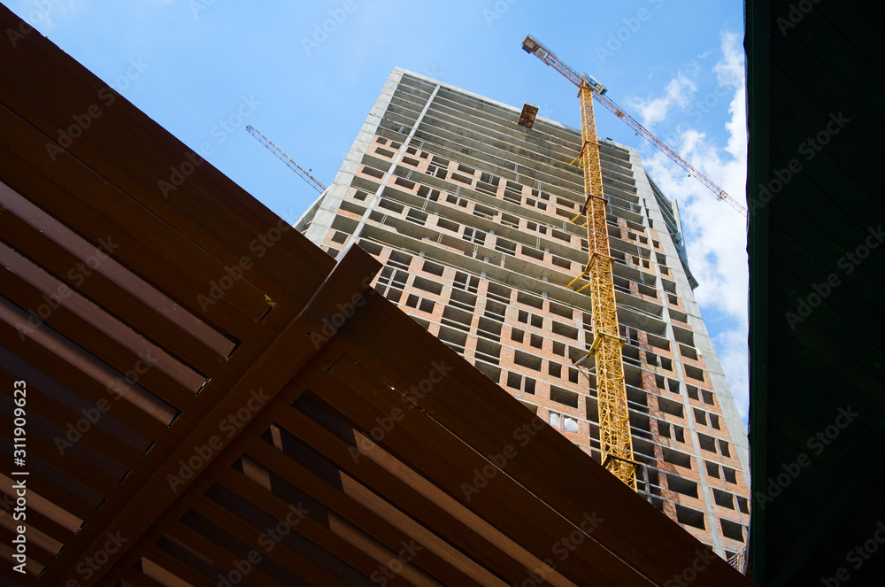 Fototapeta premium Construction site of the high skyscraper building. Building activity of modern residential building. Yellow crane machinery from low angle view. Kyiv, Ukraine.