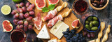 Italian antipasti wine snacks set. Prosciutto,red wine, cheese, olives, grapes, figs and cheese. Top view, banner.