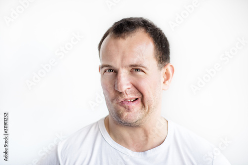 Closeup portrait of disgusted 30 years old caucasian white man on white background in white t-shirt. Man making weird face and looking in camera. Afraid, desperate, disgusted guy conceptual picture.