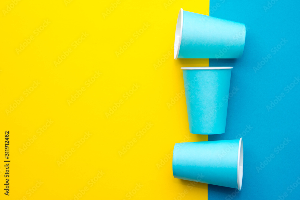 Blue paper disposable cups yellow and blue background. Cooking utensil. Cutlery sign. Top view. Minimalist Style. Copy, empty space for text Blue paper disposable cups yellow and blue background. Cooking utensil. Cutlery sign. Top view. Minimalist Style. Copy, empty space for text