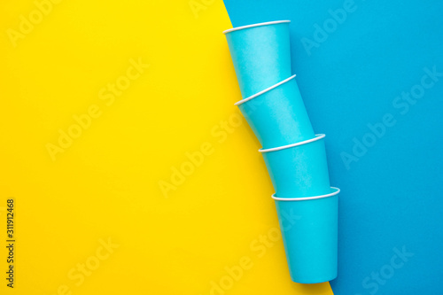 Blue paper disposable cups yellow and blue background. Cooking utensil. Cutlery sign. Top view. Minimalist Style. Copy, empty space for text © Andriy