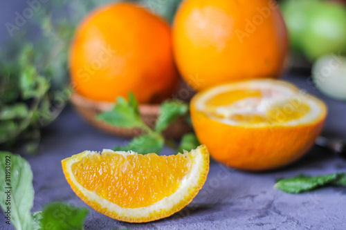 Photo of fresh orange on retro background. A slice of orange with green leaves. Half of orange on wooden plate bowl. Free space for text. Dark background. Image