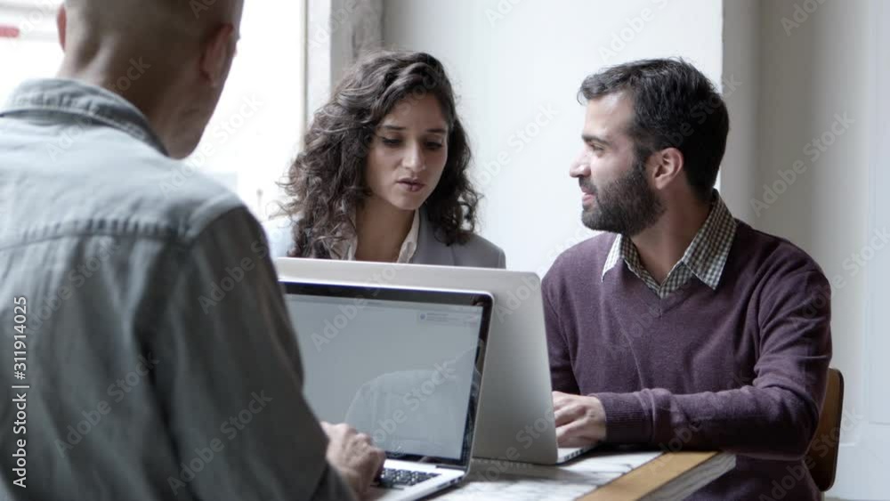 Confident employees discussing new project with laptops. Assured people sitting at table and using laptops. Technology concept Confident employees discussing new project with laptops. Assured people sitting at table and using laptops. Technology concept