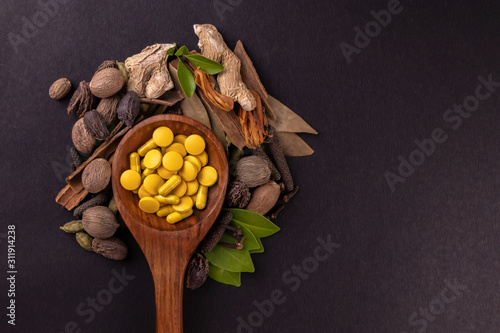 Alternative medicine concept. Close-up view of yellow herbal drugs in a wooden spoon and different spices on black background with copy space photo