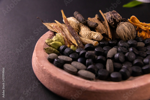 Front closeup shot of black herbal pills, spices and herbs on a grinding stone with black background photo