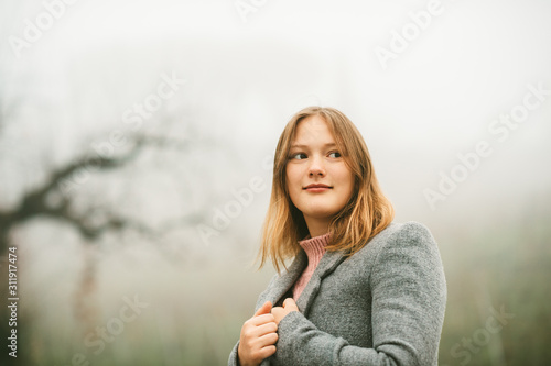 Outdoor portrait of young teenage girl on a very foggy day, wearing grey coat