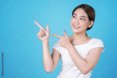 Portrait beautiful young asian woman happiness standing finger pointing something on blue blackground.