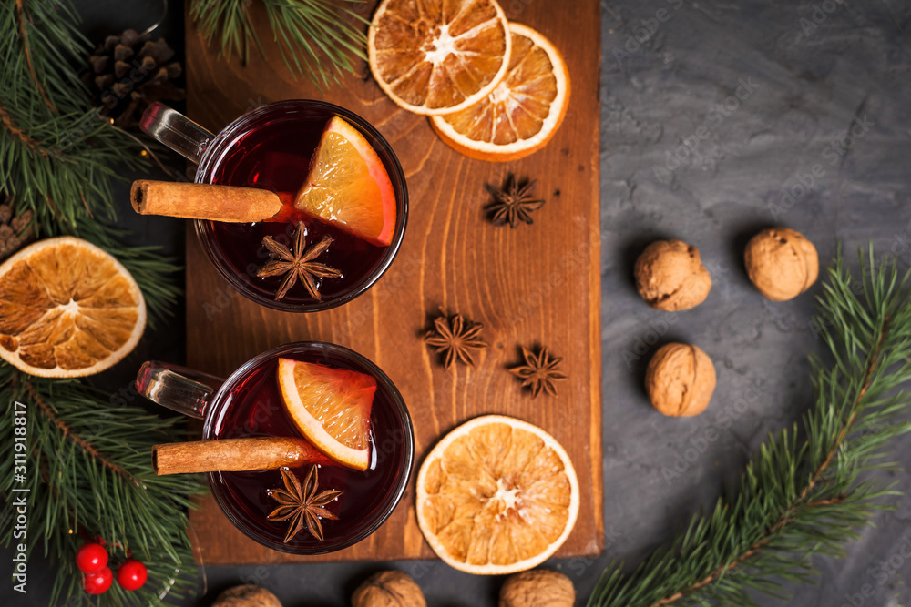 Red spicy Christmas mulled wine in two glasses with orange slices on the basis of red wine with spicy cinnamon sticks, star anise, on a black background. The view from the top.
