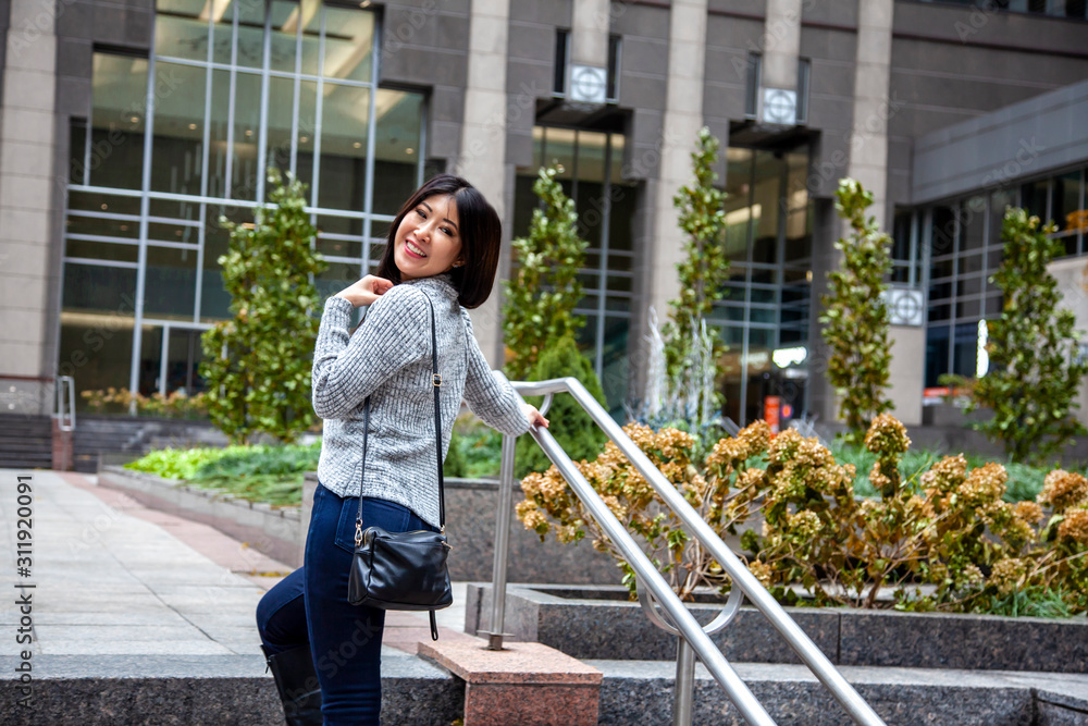 Chicago,IL/USA- November 10th 2019:a happy Asian business woman with long black hair wearing a comfortable trendy fall sweater is walking confidently carrying a fashionable handbag in downtown area