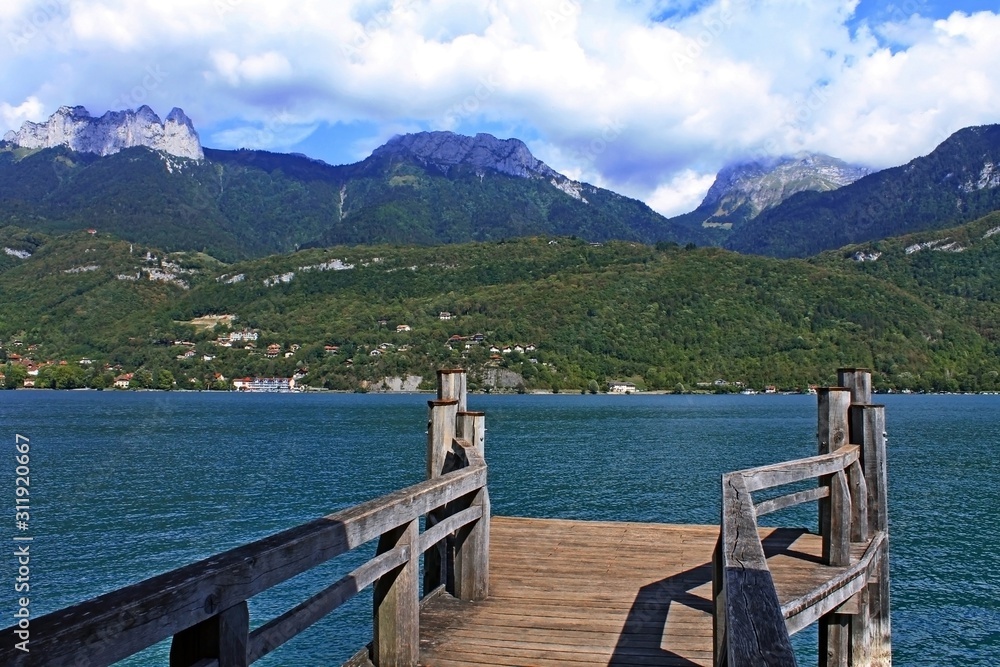 Wooden pier on Lake Annecy and the view of the opposite picturesque coast surrounded by the green Alps in France