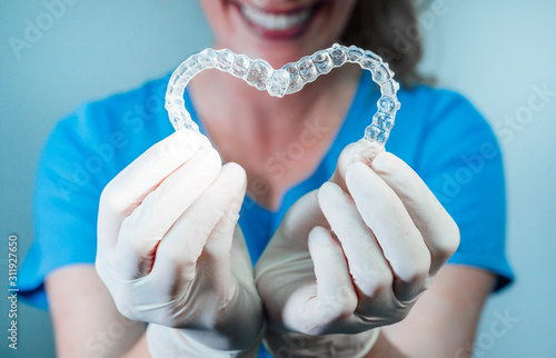 Female doctor holding two transparent heart-shaped dental aligners photo