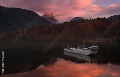 Obraz na płótnie Autumn Landscape With Two White Boats Of The Rescue Service Against The Backdrop Of The Reflection Of Triglav Mountains, Fiery Red Beech Forest And Enchanting Pink Dawn Sky. Lake Bohinj, Slovenia. w salonie