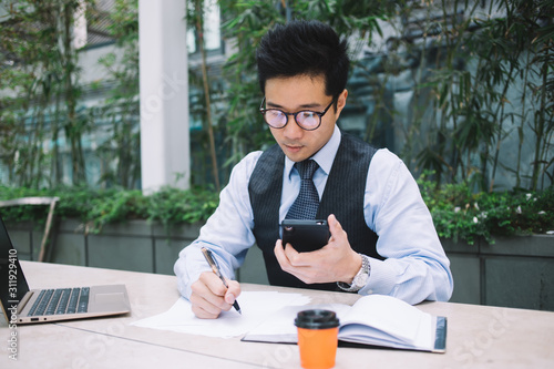 Asian man in tie and suit taking notes in notebook