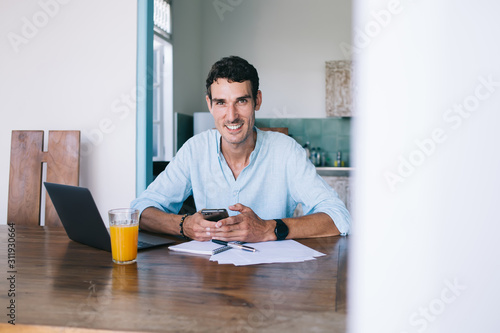 Cheerful confident businessman using smartphone and sitting at table