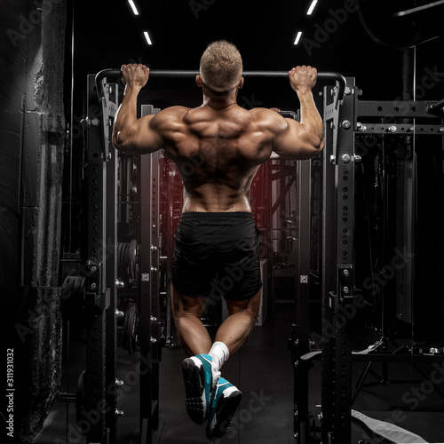 power muscular bodybuilder guy doing pullups in gym. Fitness man pumping up lats muscles. Fitness and bodybuilding training health lifestyle concept