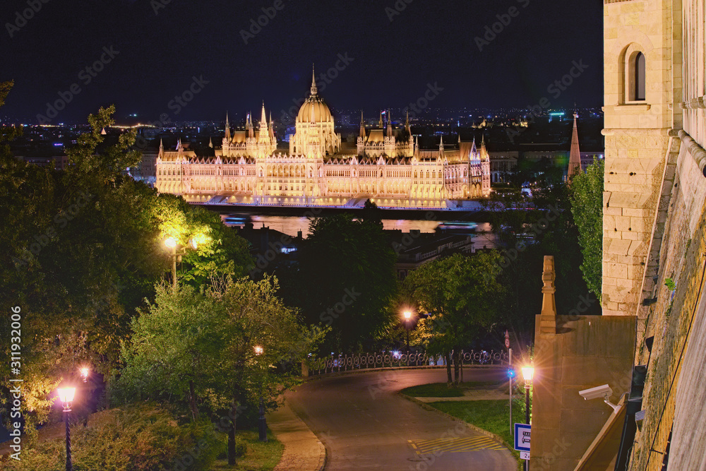 Night lights landscape of Budapest. Astonishing view of illuminated Hungarian Parliament Building. View from Fisherman's Bastion. Winding road with lanterns through the park in the foreground